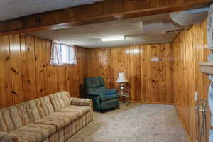 Carpeted living room with a textured ceiling and wood walls & fireplace