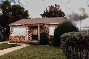 Ranch-style house featuring a front lawn, a shingled roof, stone siding, and a chimney