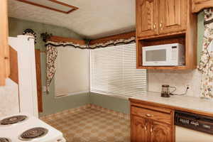 Kitchen featuring light countertops,oak cabinets, lofted ceiling, a textured ceiling, and white appliances