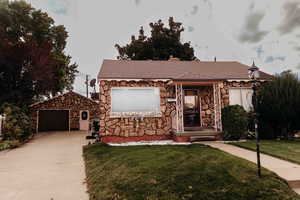 View of front of house featuring stone siding, a front lawn, roof with shingles, a chimney, and concrete driveway