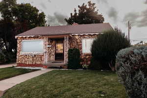 Single story home with a front yard, stone siding, roof with shingles, and a chimney