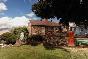 Back of property featuring stone siding, a chimney, and roof with shingles