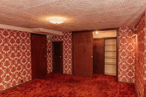 Bedroom with wallpapered walls, dark colored carpet, a large  closet, and a textured ceiling