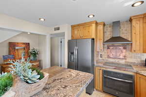 Kitchen featuring tasteful backsplash, oven, stainless steel fridge, wall chimney range hood, and recessed lighting