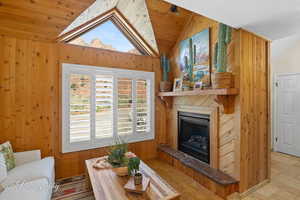 Living room with vaulted ceiling, wooden ceiling, wooden walls, and a fireplace with raised hearth