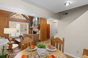 Dining space featuring a fireplace, wood walls, a chandelier, and vaulted ceiling