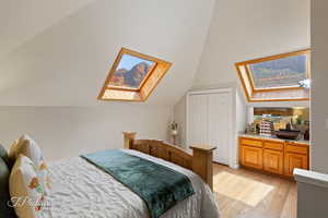 Bedroom with a skylight, light wood-type flooring, lofted ceiling, and a closet