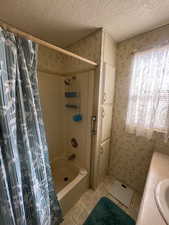 Bathroom with wallpapered walls, a textured ceiling, shower / bath combo, vanity, and light tile patterned floors