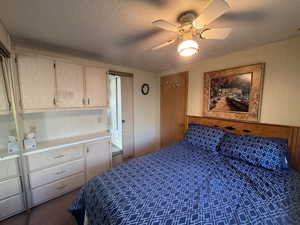 Bedroom featuring wooden walls, a textured ceiling, dark colored carpet, and ceiling fan