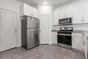 Kitchen with appliances with stainless steel finishes, white cabinets, and light stone countertops