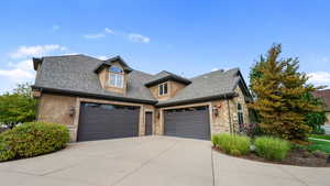 View of front of home with roof with shingles, concrete driveway, an attached garage, and stone siding