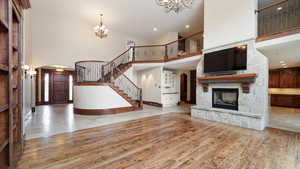 Unfurnished living room with arched walkways, a towering ceiling, light wood-type flooring, a chandelier, and a stone fireplace