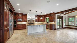 Kitchen featuring glass insert cabinets, decorative backsplash, stone tile floors, dark stone countertops, and beam ceiling