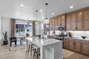 Kitchen with light wood-style flooring, a center island with sink, brown cabinets, a breakfast bar, and recessed lighting
