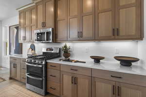 Kitchen with appliances with stainless steel finishes, backsplash, light stone countertops, light wood-style floors, and brown cabinetry