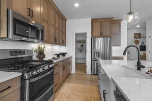 Kitchen with appliances with stainless steel finishes, pendant lighting, light stone counters, tasteful backsplash, and light wood-style floors