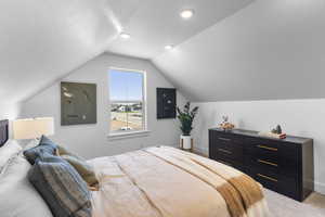 Bedroom with light colored carpet, lofted ceiling, and a textured ceiling