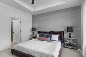 Bedroom featuring light carpet, a tray ceiling, and a ceiling fan