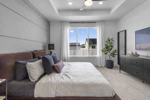 Carpeted bedroom featuring a raised ceiling, a ceiling fan, and recessed lighting