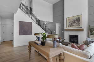 Living room featuring a towering ceiling, stairway, a chandelier, wood finished floors, and a glass covered fireplace