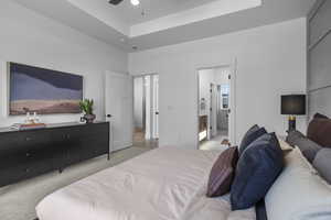 Bedroom with light carpet, a tray ceiling, ensuite bath, and a ceiling fan