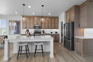 Kitchen featuring stainless steel appliances, a kitchen bar, hanging light fixtures, recessed lighting, and a kitchen island with sink