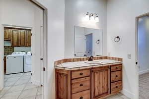 Bathroom with light tile patterned floors, vanity, decorative backsplash, and independent washer and dryer