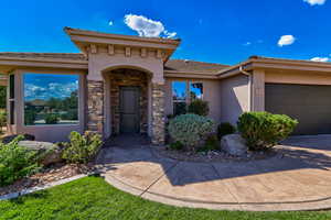 Property entrance featuring stucco siding, stone siding, a garage, and driveway