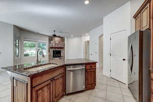 Kitchen featuring brown cabinetry, dark stone countertops, a kitchen island with sink, ceiling fan, and appliances with stainless steel finishes