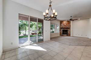 Unfurnished living room featuring light tile patterned floors, a chandelier, a stone fireplace, a ceiling fan, and recessed lighting