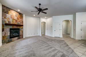 Unfurnished living room with light tile patterned flooring, a large fireplace, light colored carpet, recessed lighting, and a ceiling fan