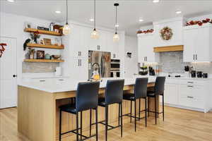 Kitchen with an island with sink, decorative backsplash, open shelves, a breakfast bar, and hanging light fixtures