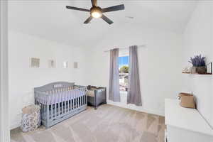 Bedroom with light carpet, a crib, ceiling fan, and high vaulted ceiling