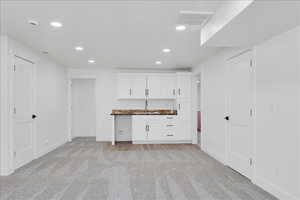 Kitchen featuring recessed lighting, light colored carpet, white cabinetry, and wood counters