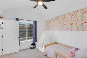 Bedroom featuring a wainscoted wall, wallpapered walls, carpet flooring, lofted ceiling, and ceiling fan