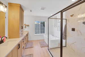 Bathroom with a freestanding bath, double vanity, a marble finish shower, and light wood-type flooring