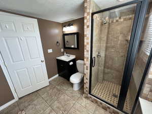 Bathroom with vanity, a stall shower, a textured ceiling, and light tile patterned floors