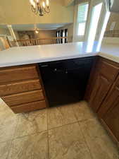 Kitchen with brown cabinets, light countertops, black dishwasher, and a chandelier