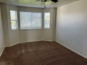 Carpeted empty room with a textured ceiling and a ceiling fan