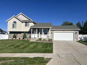 Tri-level home with stone siding, a porch, driveway, an attached garage, and stucco siding