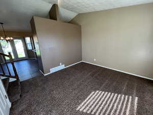 Tiled empty room featuring lofted ceiling, carpet, a chandelier, stairway, and a textured ceiling