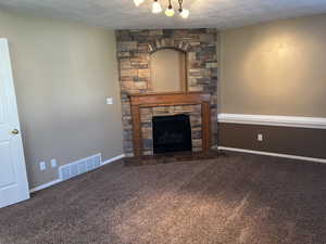 Unfurnished living room featuring a fireplace, a textured ceiling, and dark carpet
