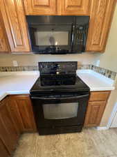 Kitchen with black appliances, light countertops, and brown cabinetry