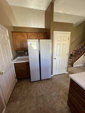 Kitchen with light countertops, freestanding refrigerator, and brown cabinets