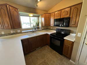 Kitchen featuring black appliances, a textured ceiling, light countertops, brown cabinets, and lofted ceiling