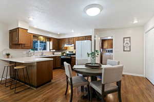 Kitchen with light countertops, freestanding refrigerator, electric stove, a kitchen breakfast bar, and dark wood-style floors
