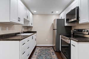 Kitchen featuring dark countertops, stainless steel appliances, dark wood-style flooring, white cabinetry, and recessed lighting