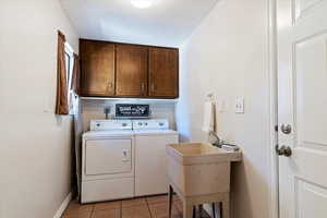 Washroom featuring light tile patterned floors, cabinet space, and washing machine and clothes dryer