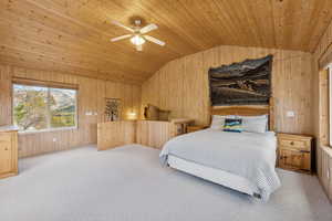 Bedroom featuring vaulted ceiling, wooden walls, carpet flooring, a ceiling fan, and wooden ceiling
