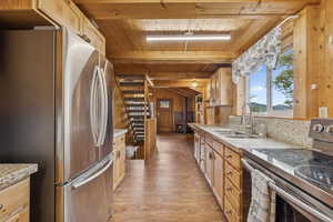 Kitchen featuring stainless steel appliances, light stone counters, wood walls, light wood-type flooring, and a wooden ceiling with exposed beams